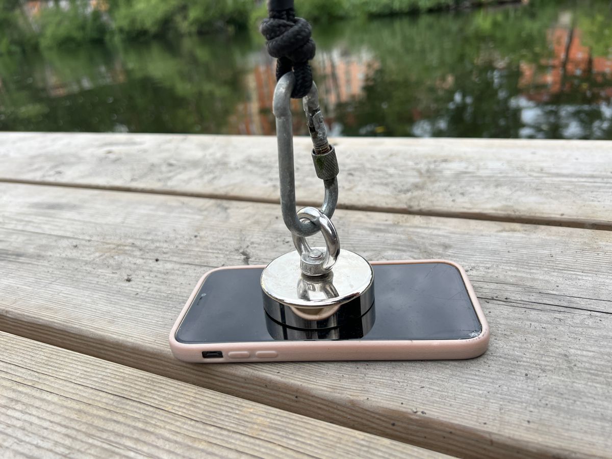 Kraftig sökmagnet i lina vilar ovanpå glaset på en mobiltelefon på en brygga.